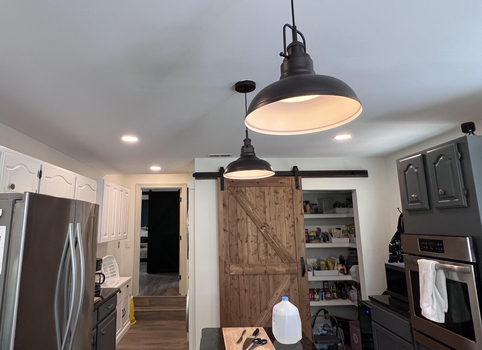 Kitchen work with wood barn door, black light fixtures, cabinets, and pantry shelving